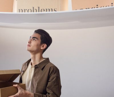 A thoughtful man indoors holding a box labeled 'kind', surrounded by words like 'problems'.