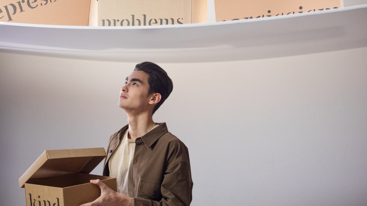 A thoughtful man indoors holding a box labeled 'kind', surrounded by words like 'problems'.